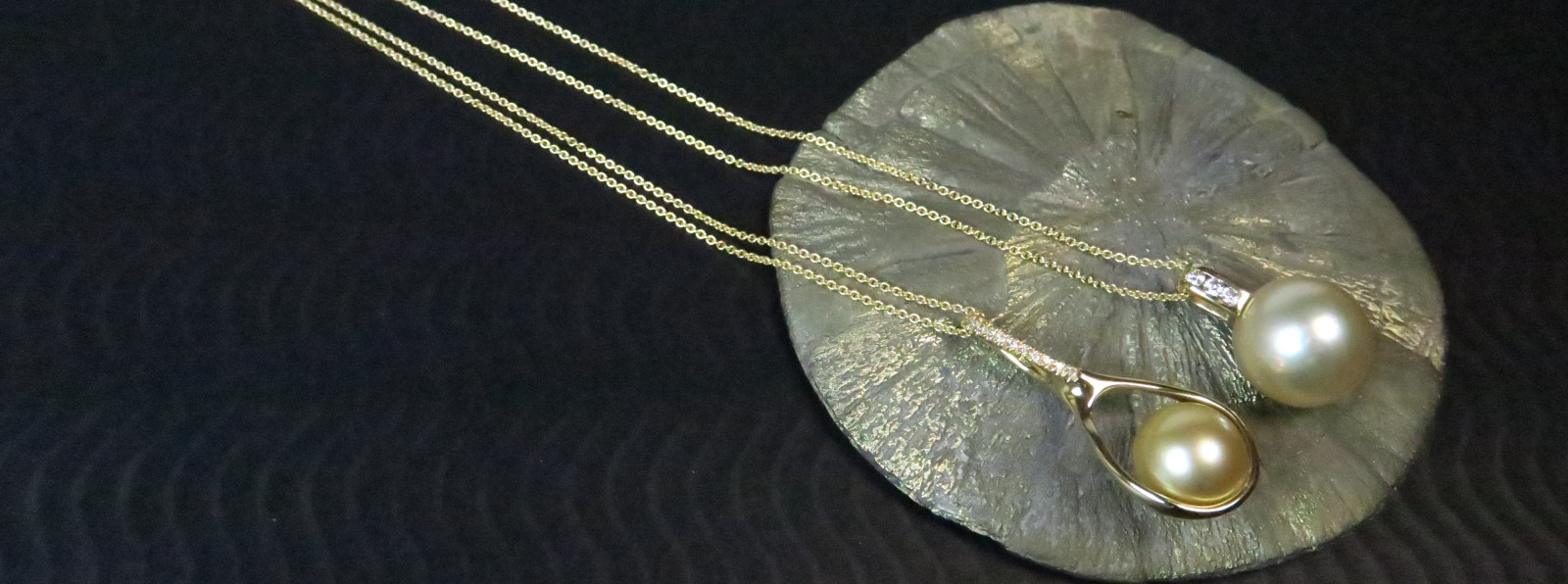 Luxuriöse goldene Südseeperlen als Halsketten an feinen Goldketten, präsentiert auf einer glänzenden Pyrit-Mineralienscheibe.