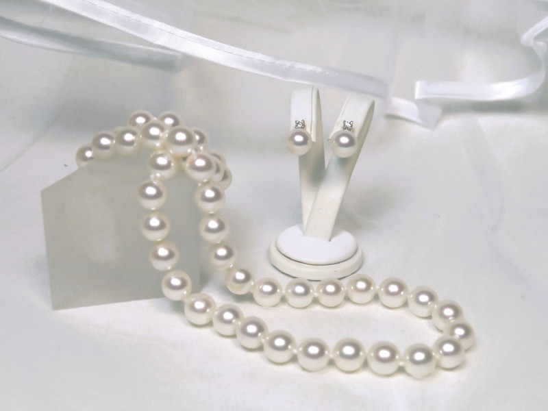 Eine strahlende Braut trägt ein edles Akoya-Perlencollier und passende Perlenohrringe als klassischen, zeitlosen Brautschmuck.