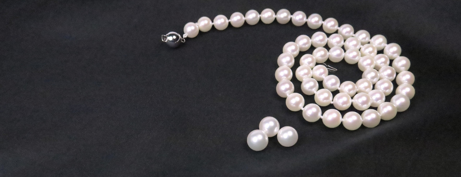 Klassische japanische Akoyaperlen als weiße Perlenkette mit makellosem, tiefem Glanz auf elegant drapiertem, dunklem Stoff.