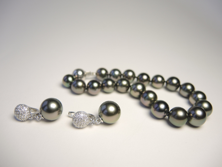 Ein Set aus eleganten Ohrringen und einem Armband mit echten, dunklen Tahitiperlen in Anthrazit mit gruen-violett schimmernden Obertoenen.
